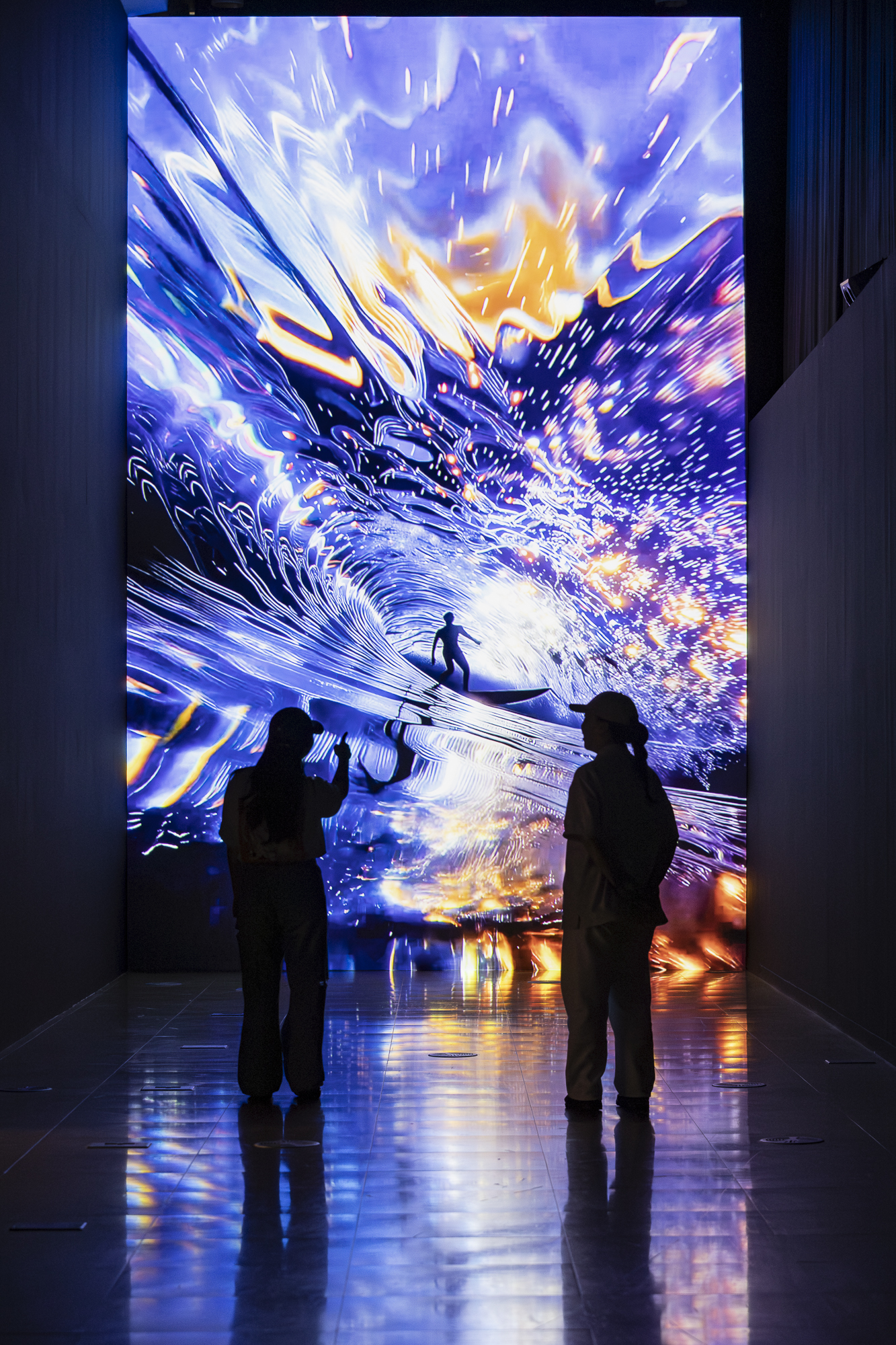 Two visitors viewing Inhwa Yeom’s Dreaming Chandra (D.C.), a luminous purple, blue, and orange media-wall video at ACC in 2025